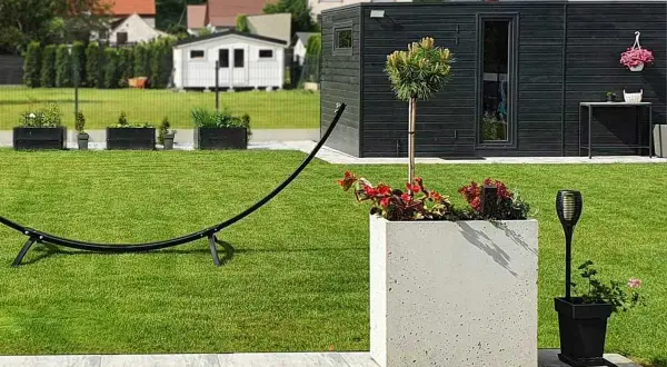 Nowoczesny ogród z zadbanym trawnikiem, betonową donicą, drzewkiem i czarną altaną.