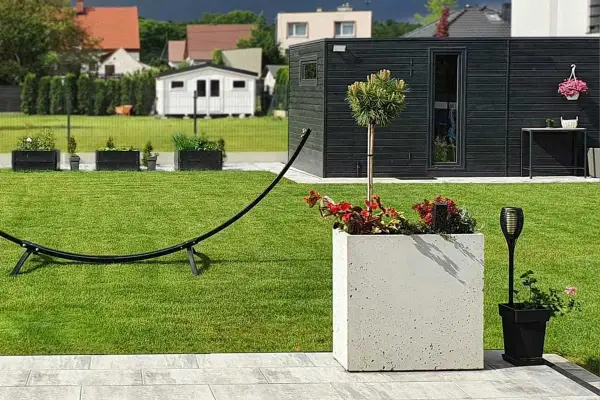 Nowoczesny ogród z zadbanym trawnikiem, betonową donicą, drzewkiem i czarną altaną.